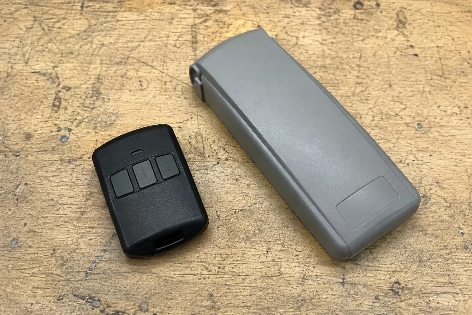 Three-button remote beside a closed grey keypad cover on a workbench. — Garage Door Remote and Keypad Programming, Mississauga