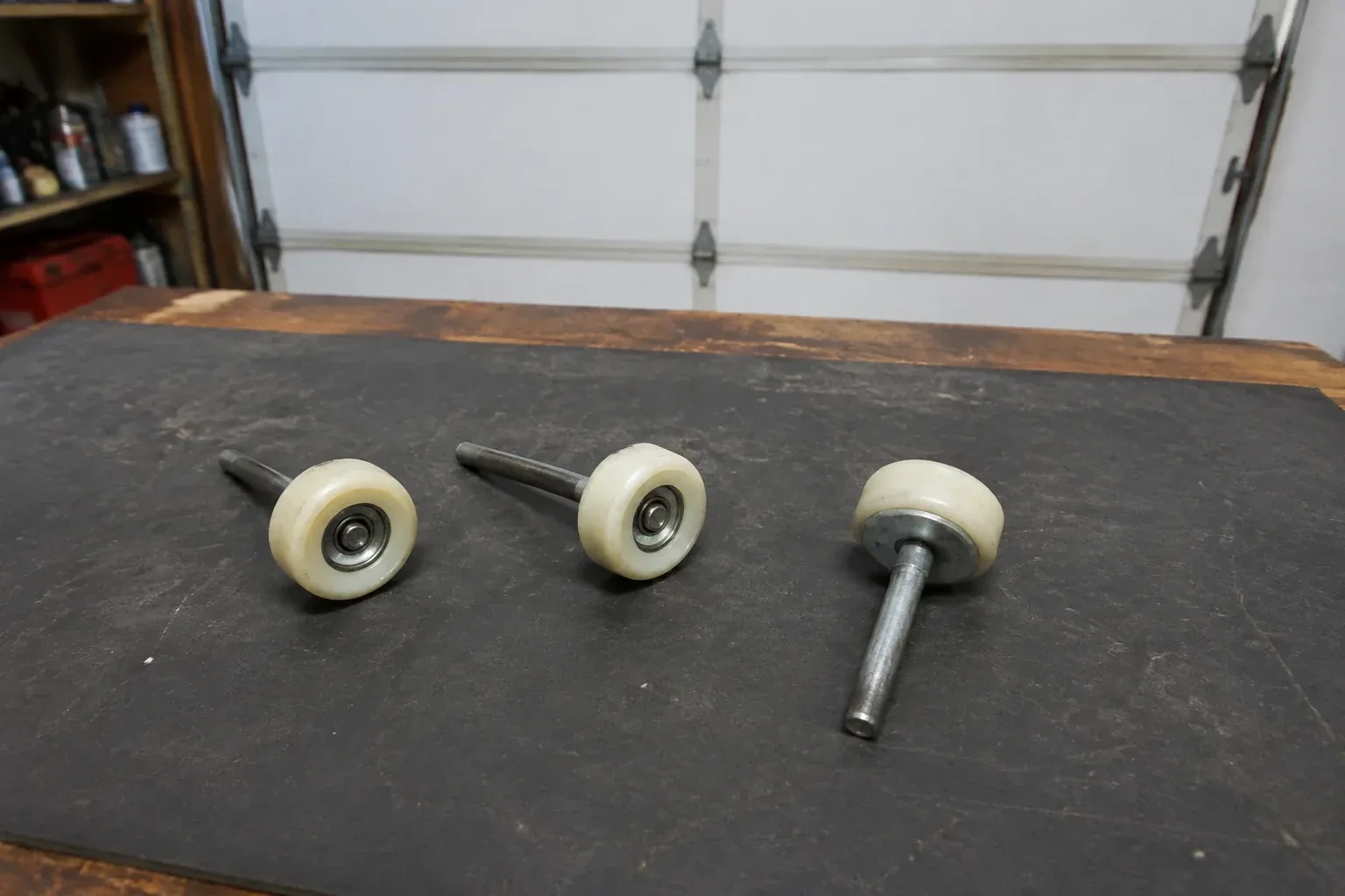Three detached nylon-wheel garage door rollers with steel stems on a work mat. — Garage Door Roller Replacement, Mississauga